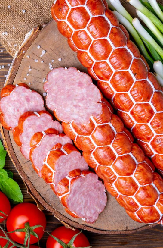Thick netted cooked and smoked beef sausage, sliced cold on a board.